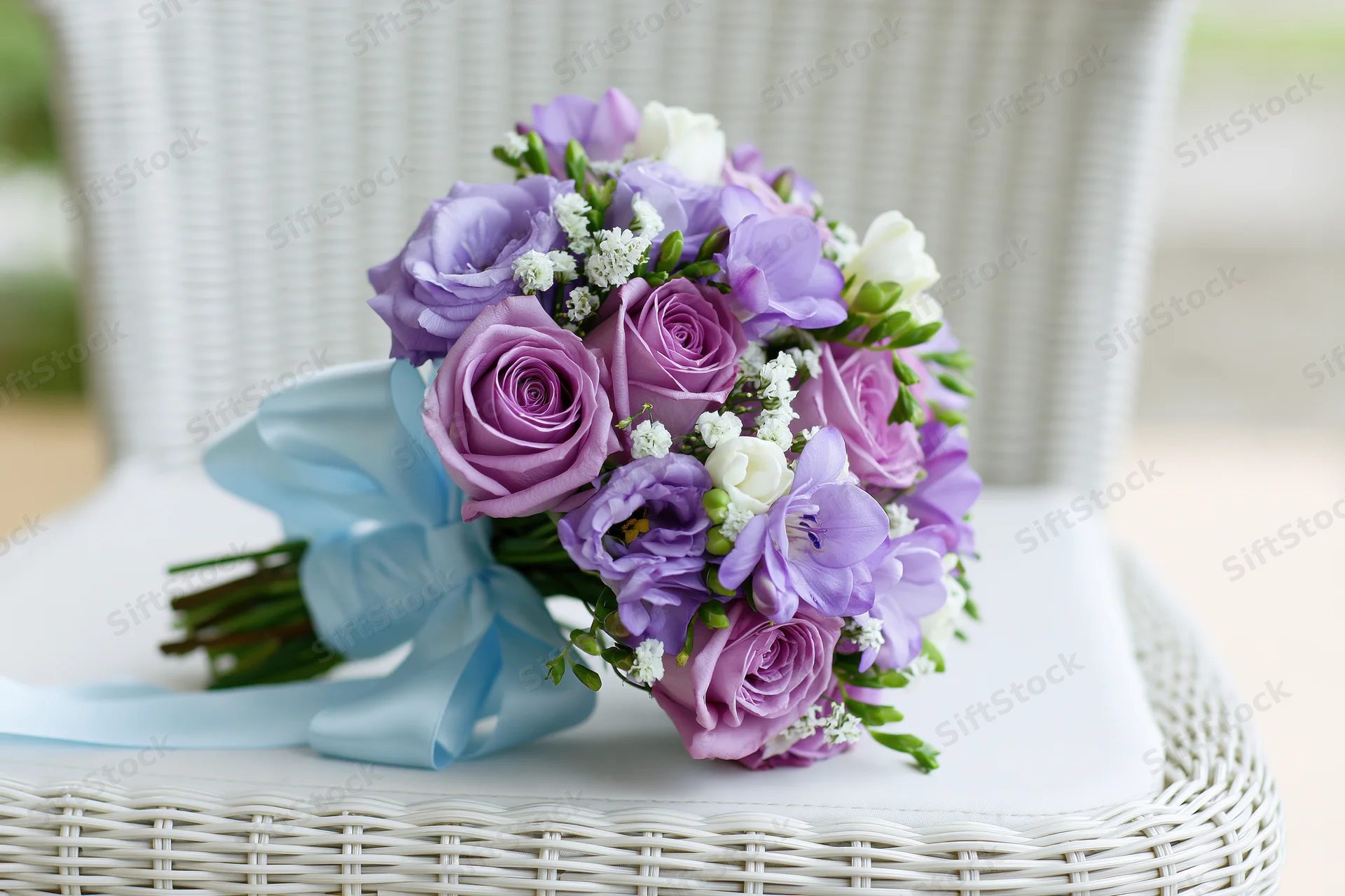 Bridal bouquet of purple roses and lavender lisianthus with white freesia on a white wicker chair