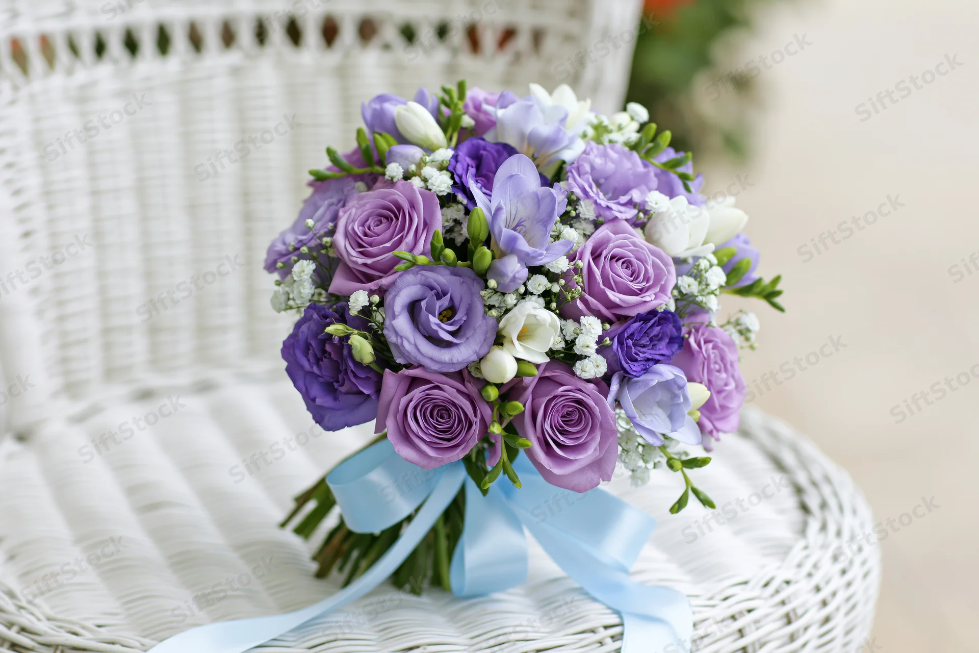 Bridal bouquet of purple roses, lavender lisianthus and freesia resting on a white wicker chair
