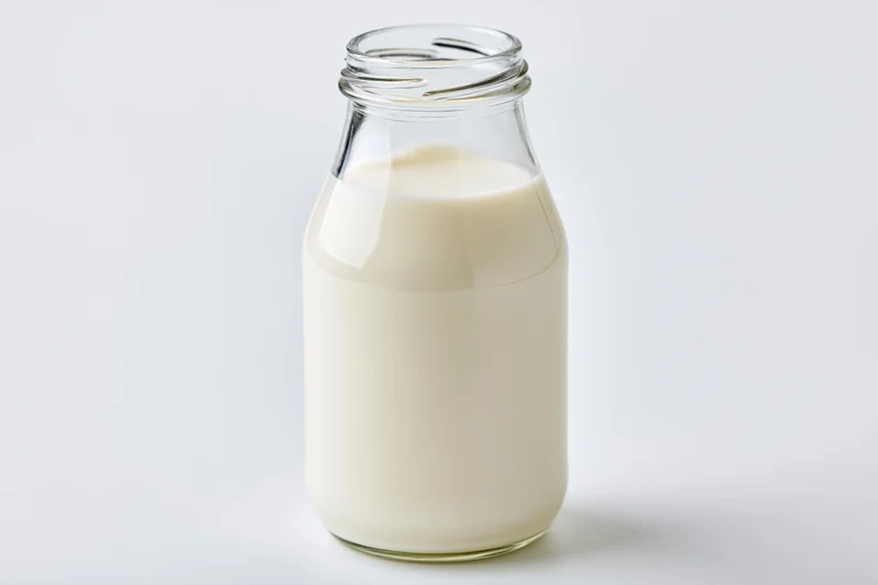 Clear glass bottle filled with fresh whole milk open on white background