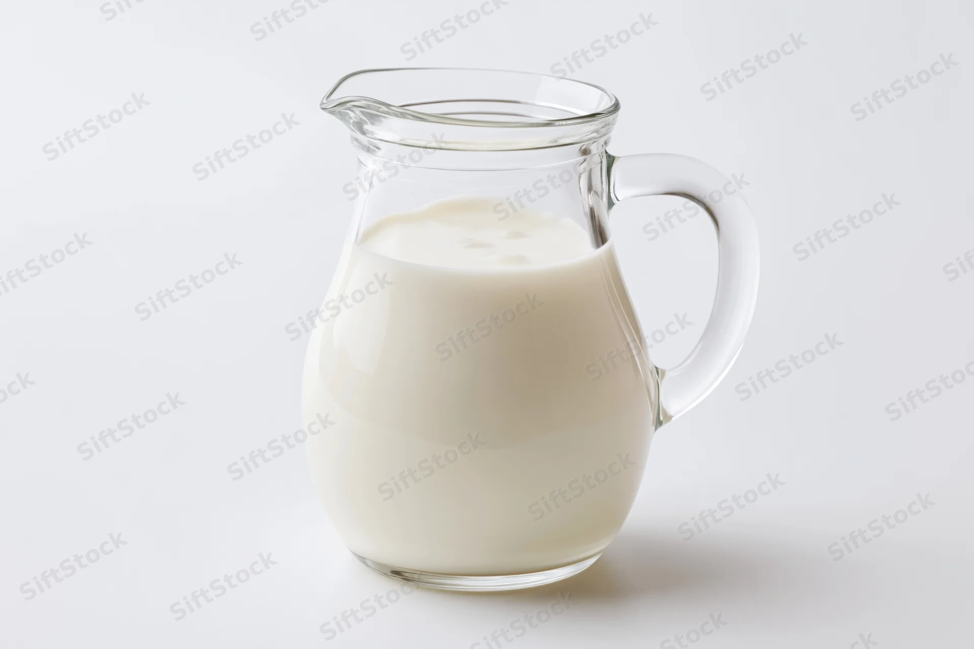 Clear glass pitcher filled with fresh whole milk on white background