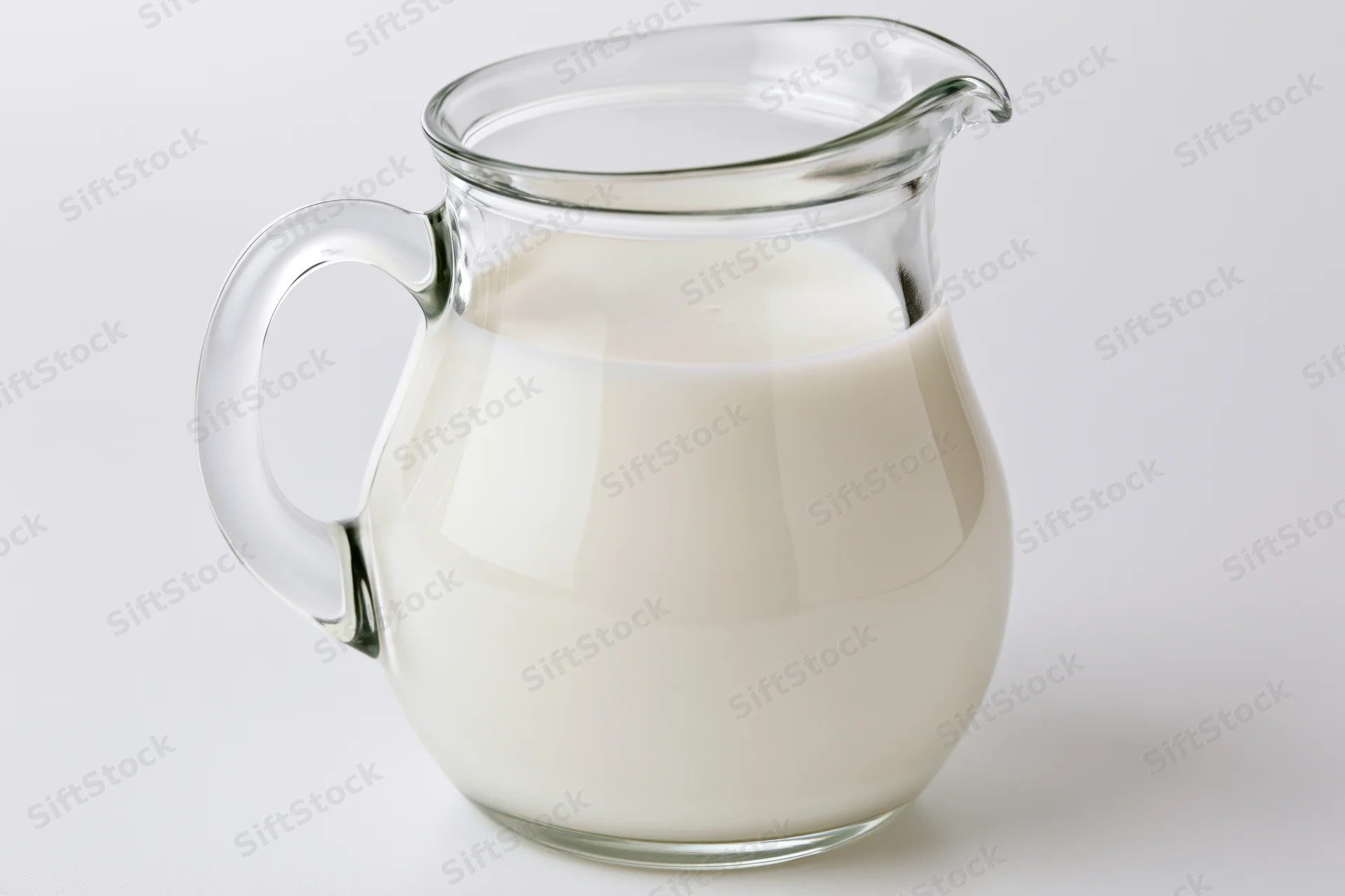 Clear glass pitcher filled with fresh whole milk on white background