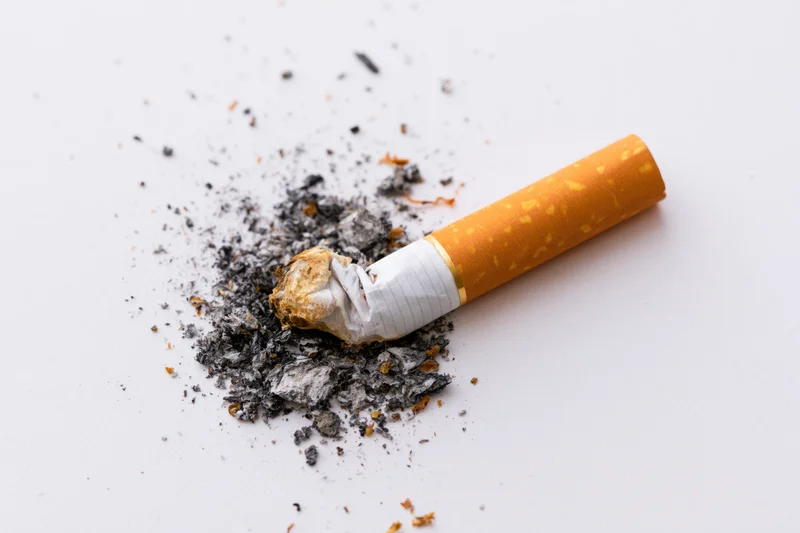 Crushed cigarette butt with ash on white surface