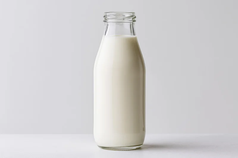 Glass bottle filled with milk standing on a white surface