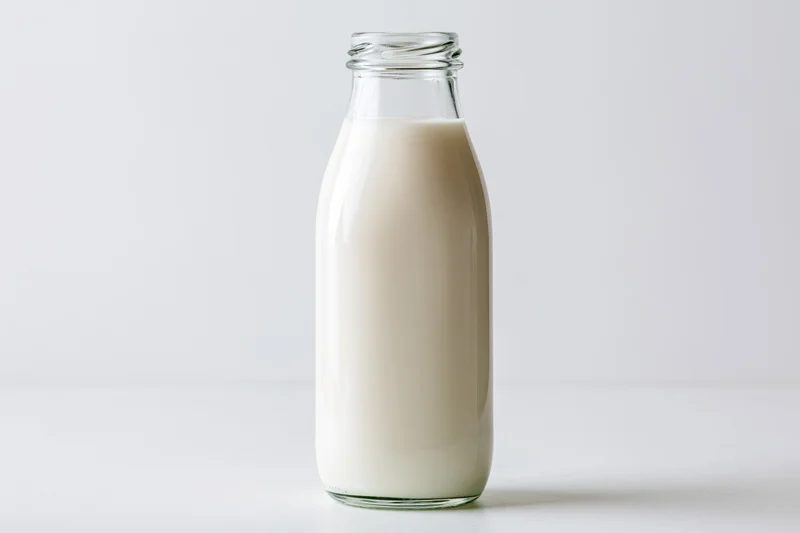 Glass bottle filled with milk standing on white surface