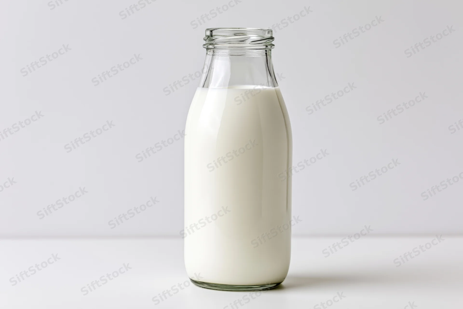 Glass milk bottle filled with white liquid standing upright on a white surface