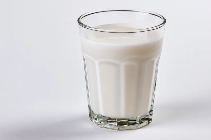 Full glass of cold milk on plain white surface