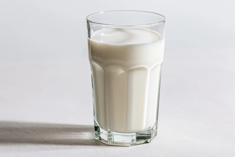 Full glass of cold milk on plain white surface