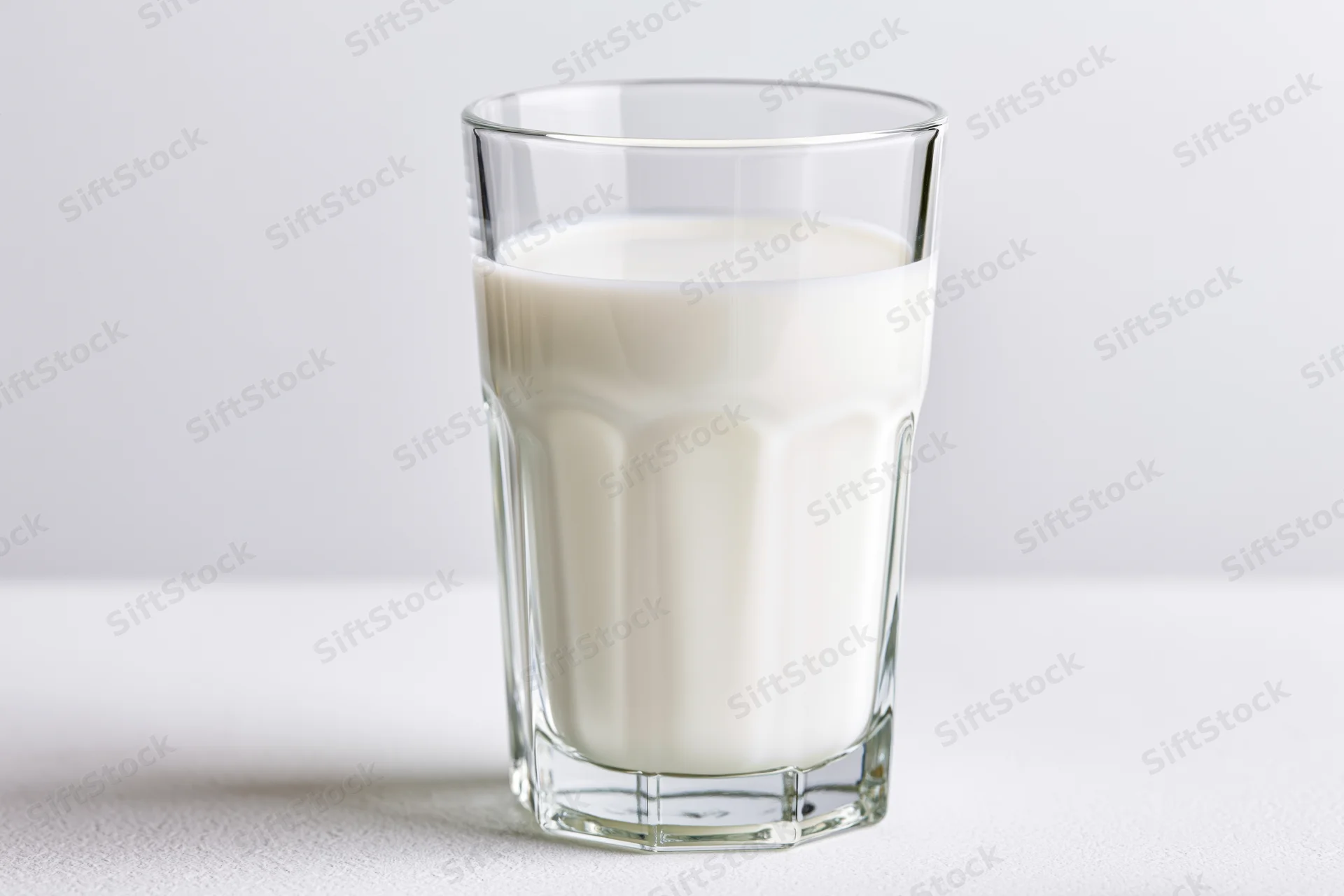 Full glass of cold milk on a plain white surface