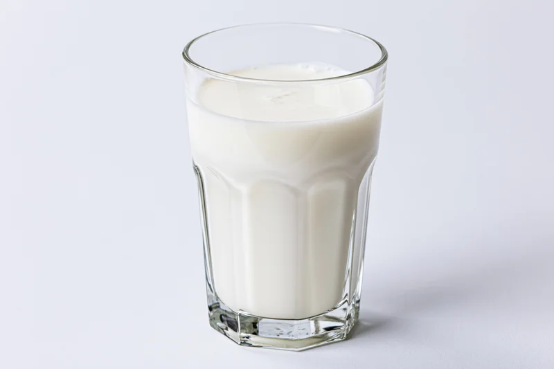 Full glass of cold milk on plain white surface