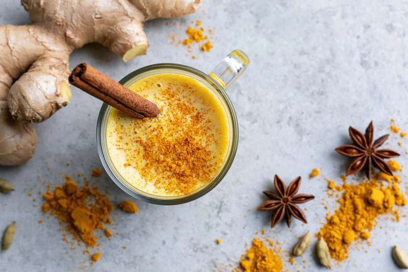 Golden turmeric latte in a glass mug with cinnamon stick and spices arranged on a light surface