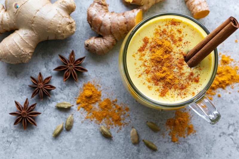 Golden turmeric latte in a glass mug with cinnamon stick and spices arranged on a gray stone surface
