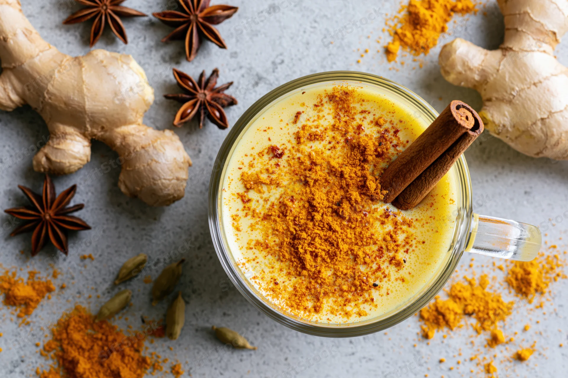 Golden turmeric latte in a glass mug with cinnamon stick and spices on countertop