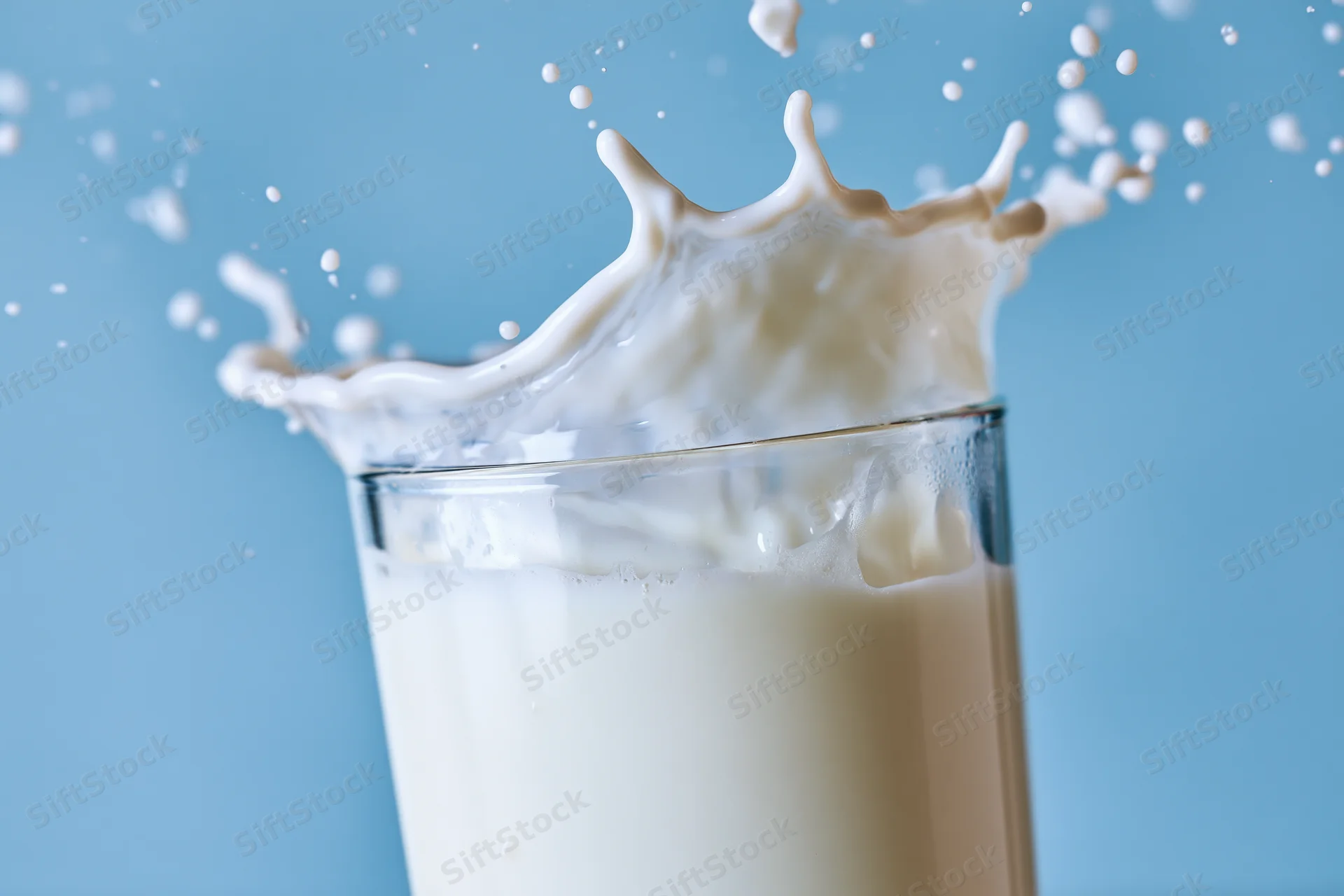 Milk splashing upward in a glass against a blue background
