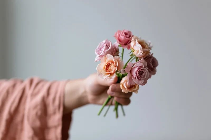 Hand holding a small bouquet of pink and peach roses against a light background