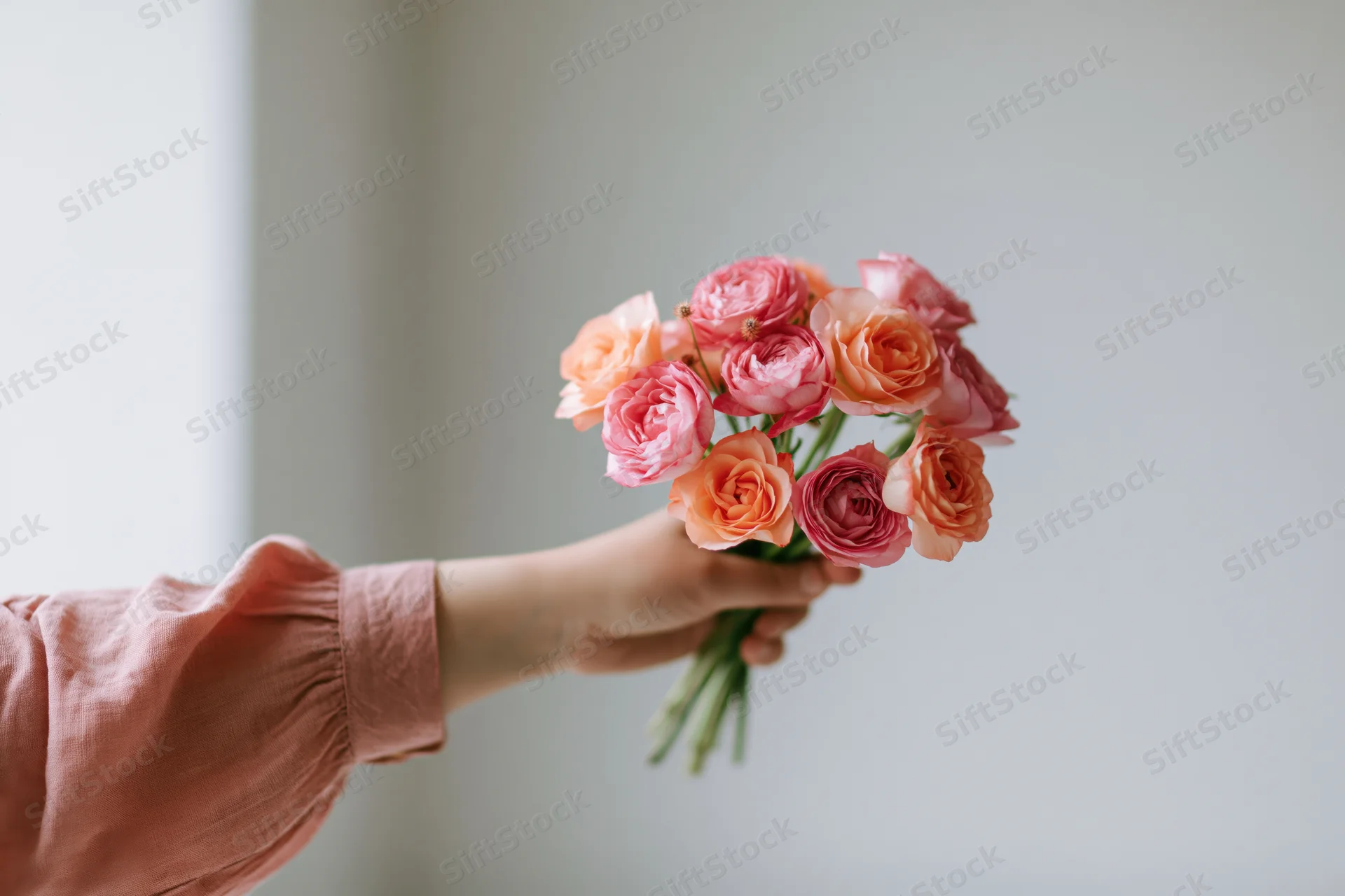 Woman's hand holding a small bouquet of pink and peach roses against a light background