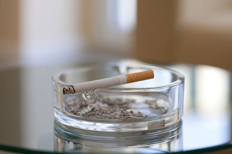 Lit cigarette resting in a glass ashtray on a reflective table