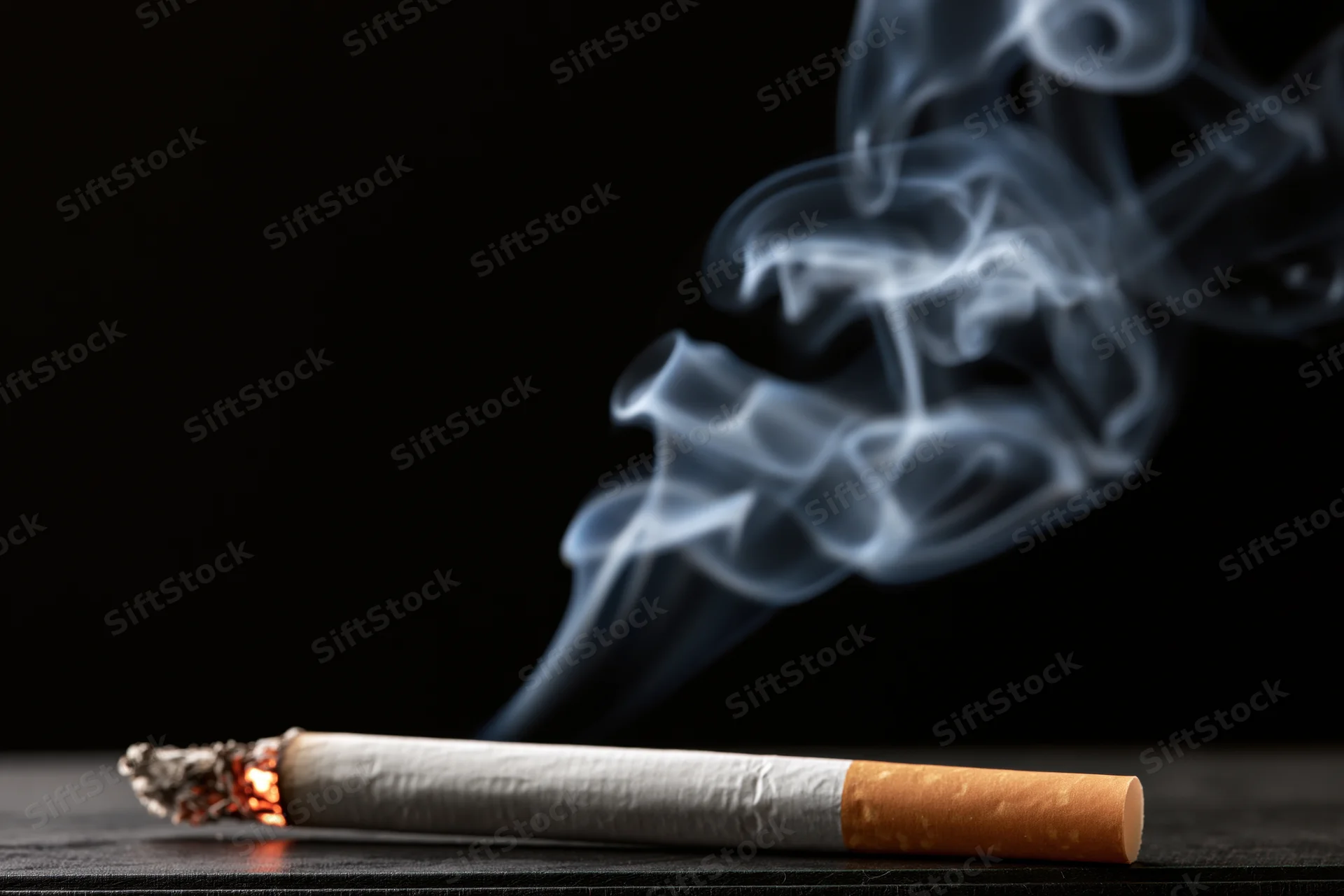Lit cigarette with rising smoke on dark surface