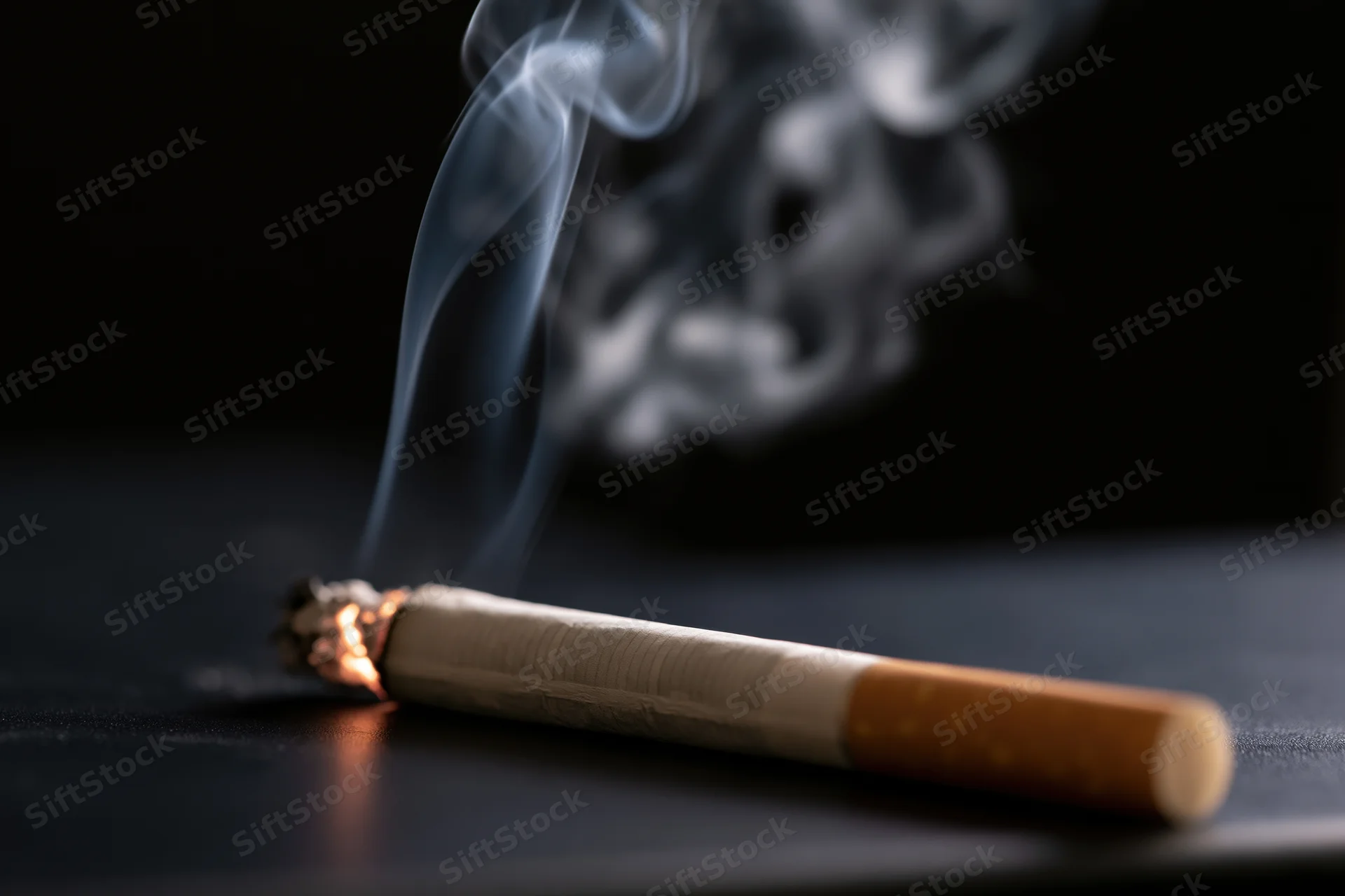 Lit cigarette burning on dark surface with rising smoke