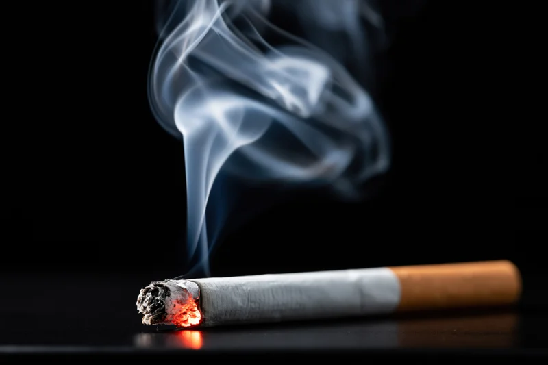 Lit cigarette with rising smoke resting on dark surface
