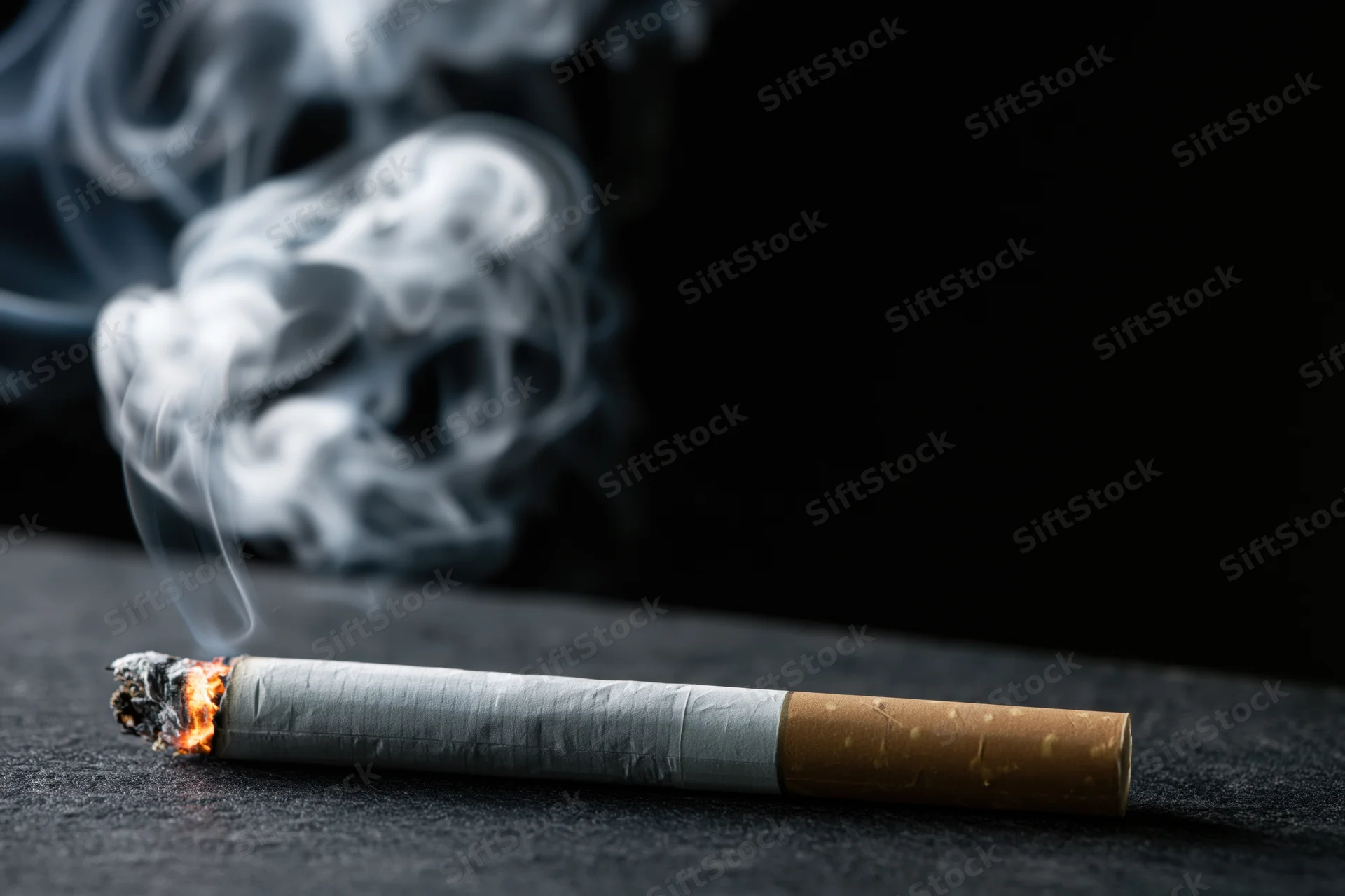 Lit cigarette burning on dark surface with rising white smoke