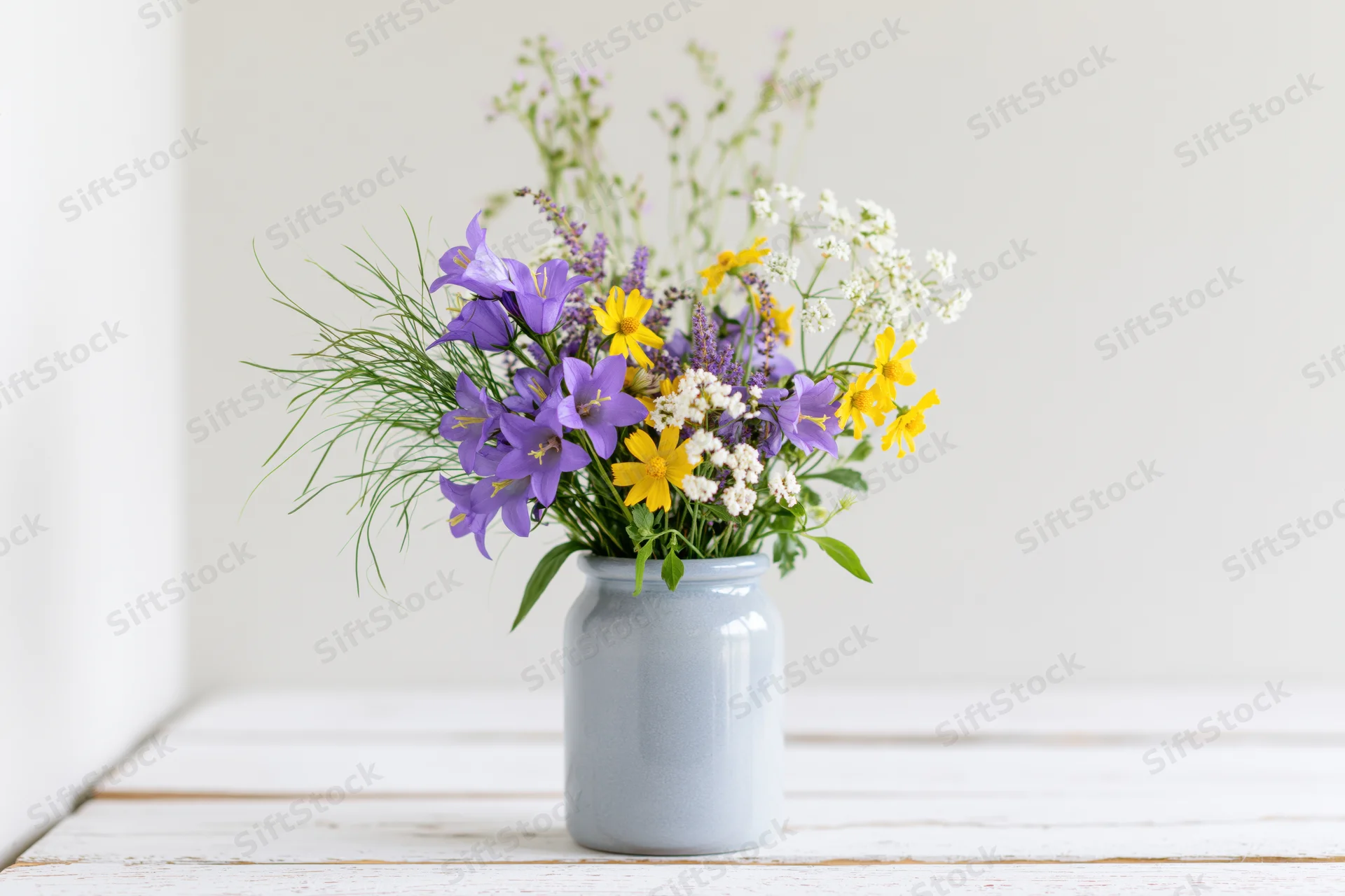 Loose bouquet of purple and yellow wildflowers in a blue ceramic vase on a white wooden table