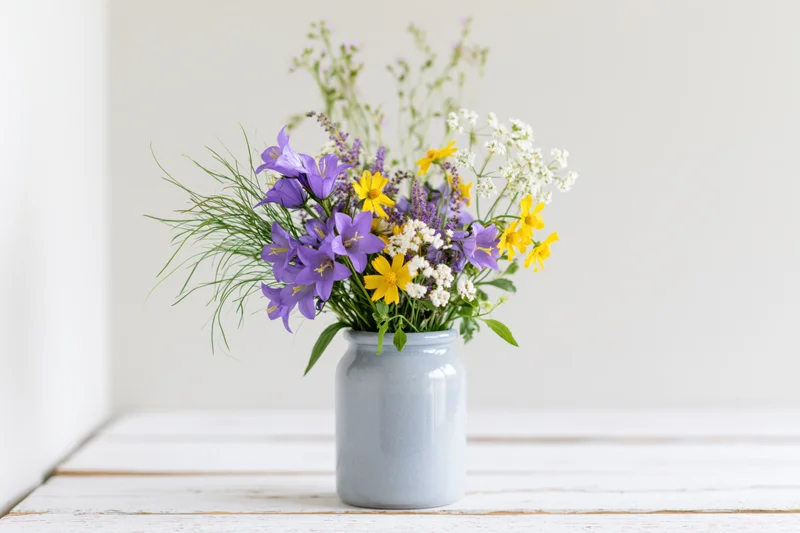 Loose bouquet of purple and yellow wildflowers in a blue ceramic vase on a white wooden table