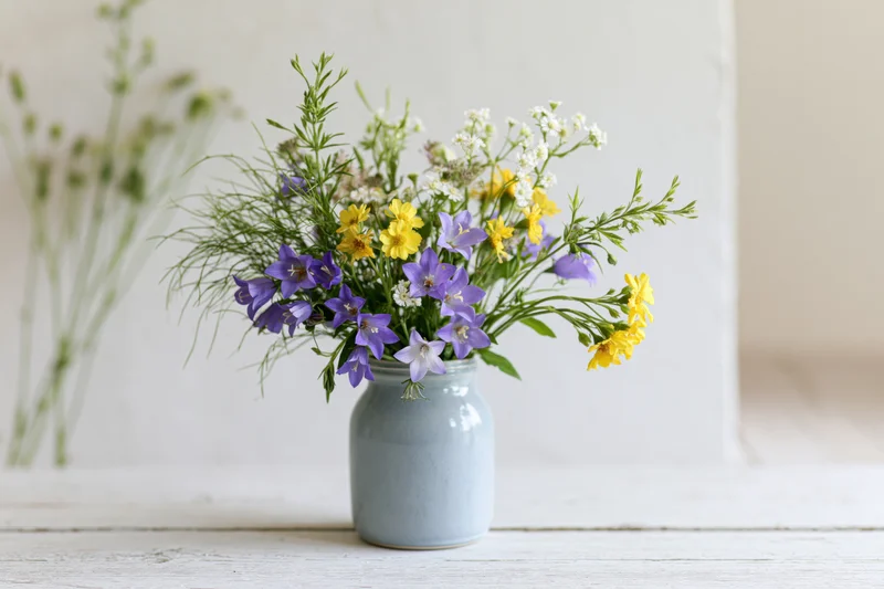 Loose bouquet of mixed wildflowers in a blue ceramic vase on a white wooden table