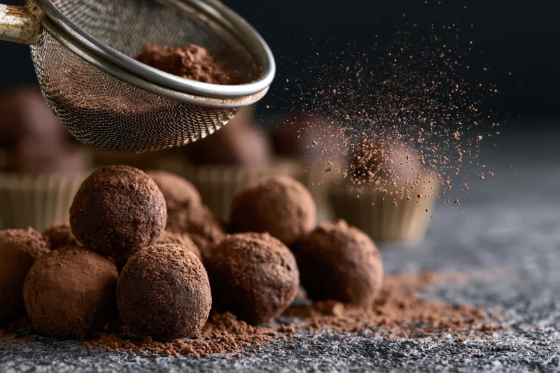 Cocoa powder sifted over chocolate truffles on a dark surface