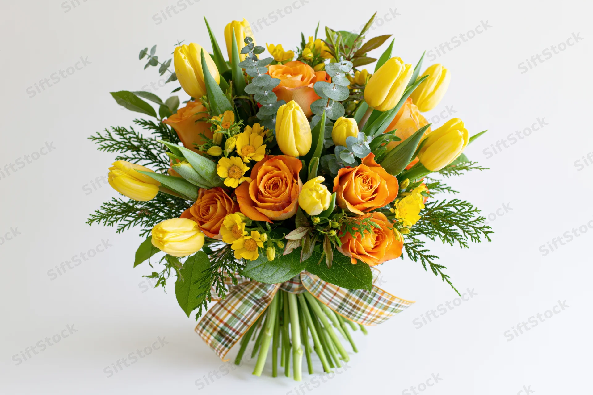 Mixed bouquet of yellow tulips and orange roses with greenery and plaid ribbon on white background