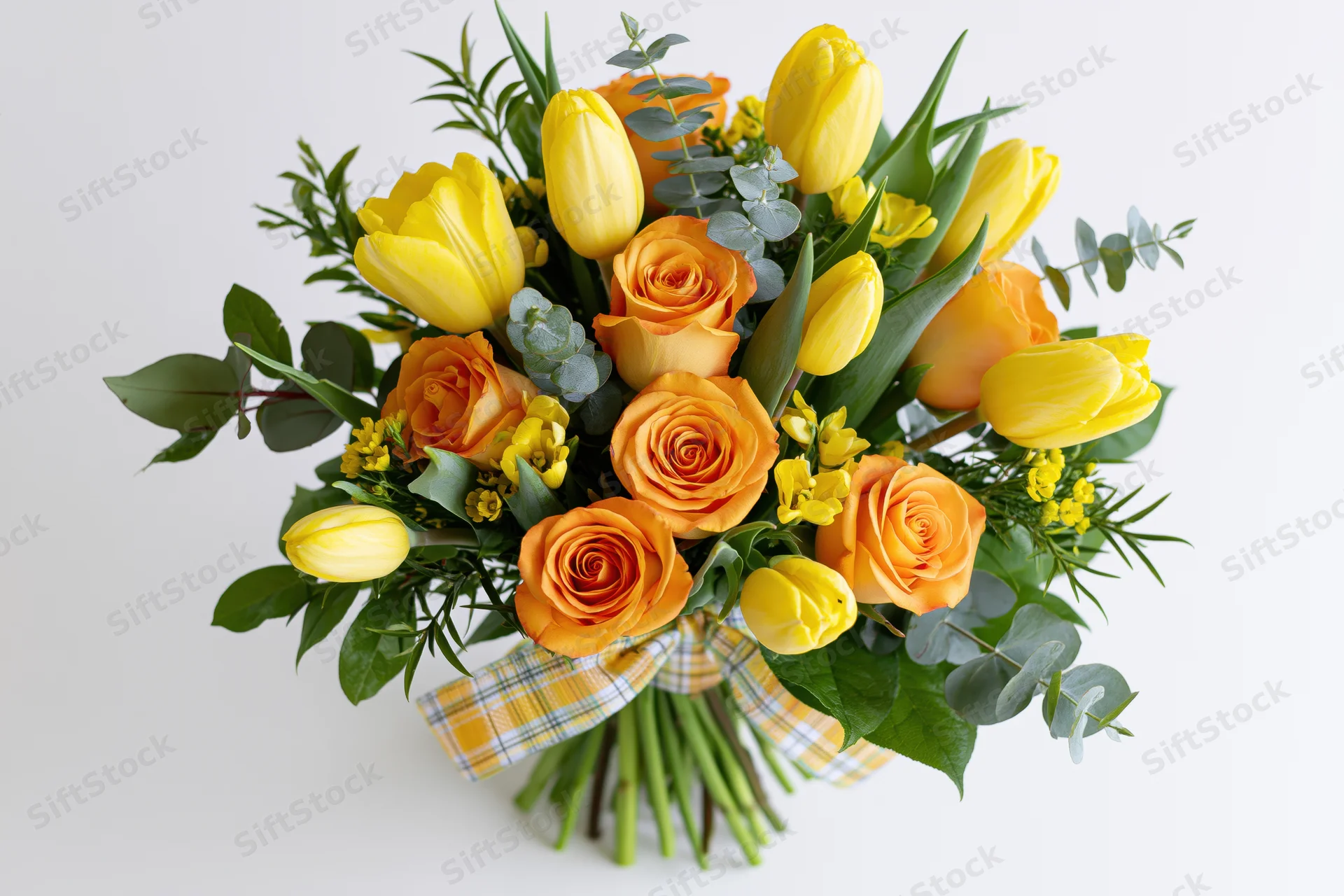 A bouquet of yellow tulips and orange roses with green foliage and a plaid ribbon on a white background