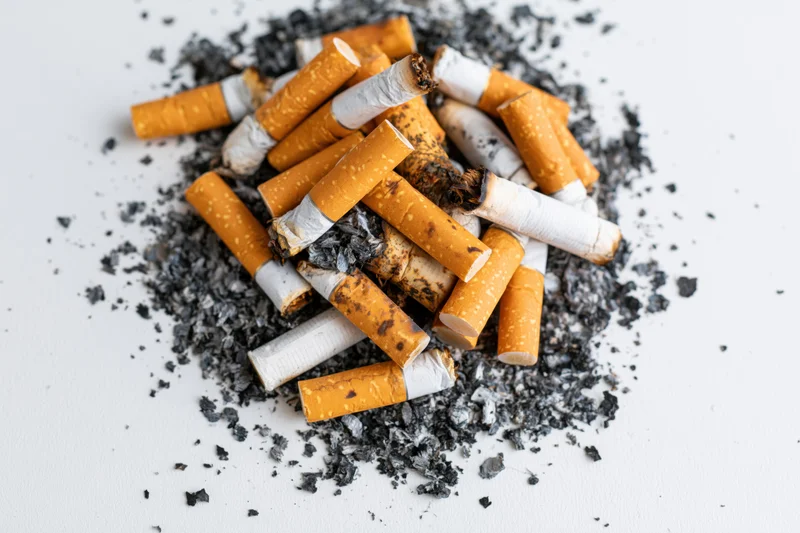 Pile of used cigarette butts and ash on white surface
