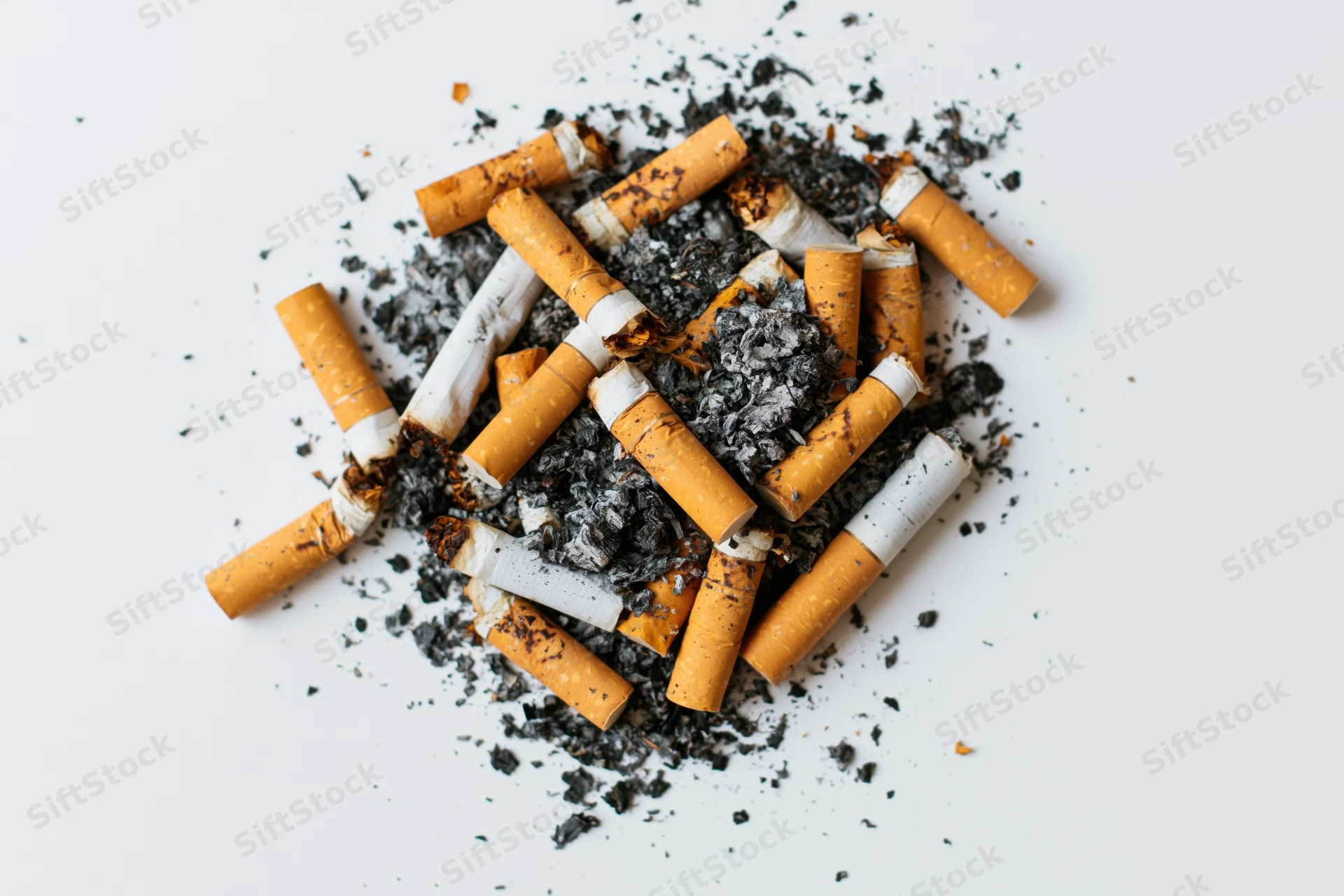 Pile of used cigarette butts with ash scattered on white surface
