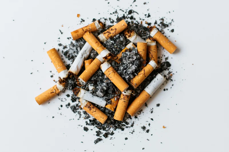 Pile of used cigarette butts with ash scattered on white surface