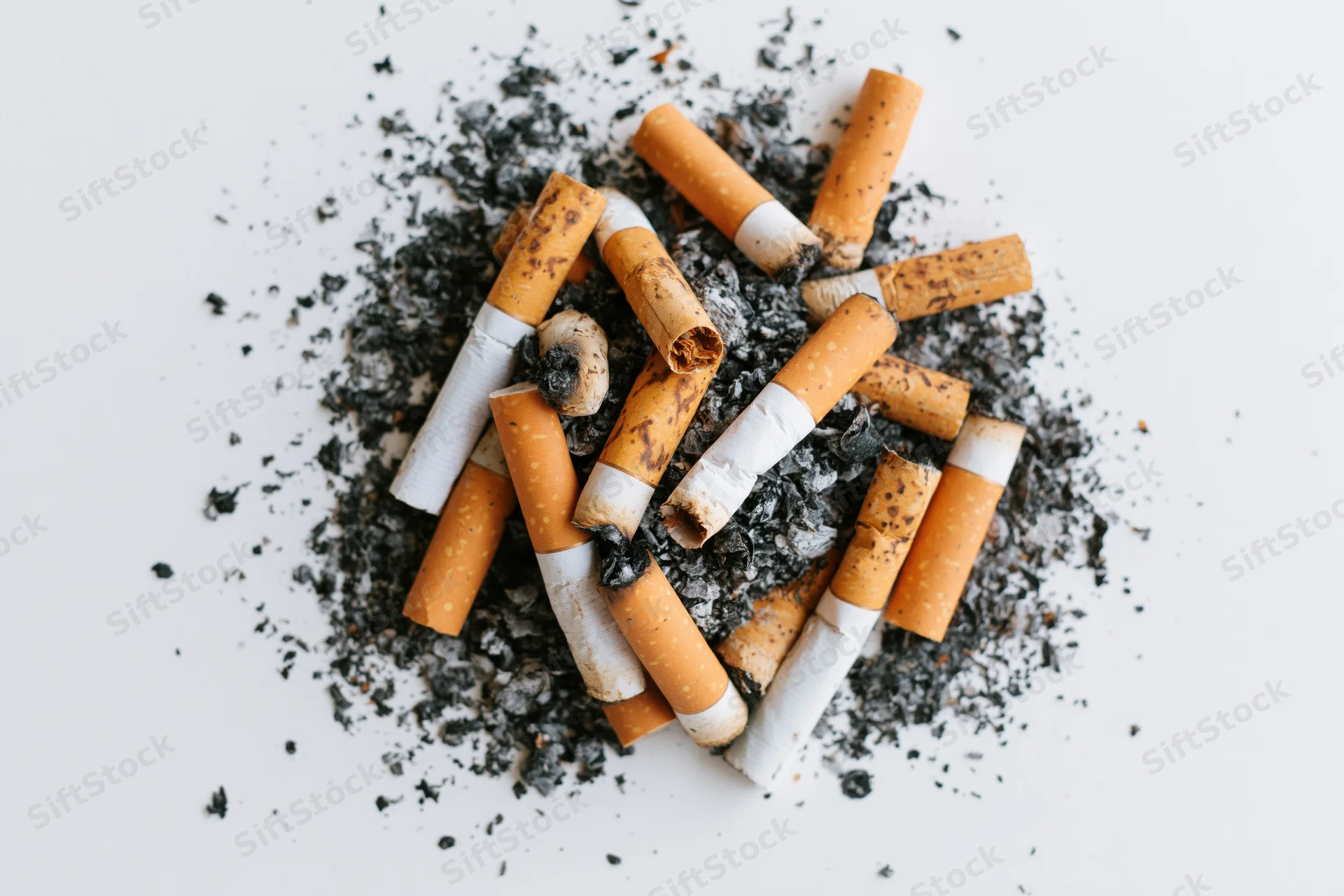 Pile of used cigarette butts and ash on white surface