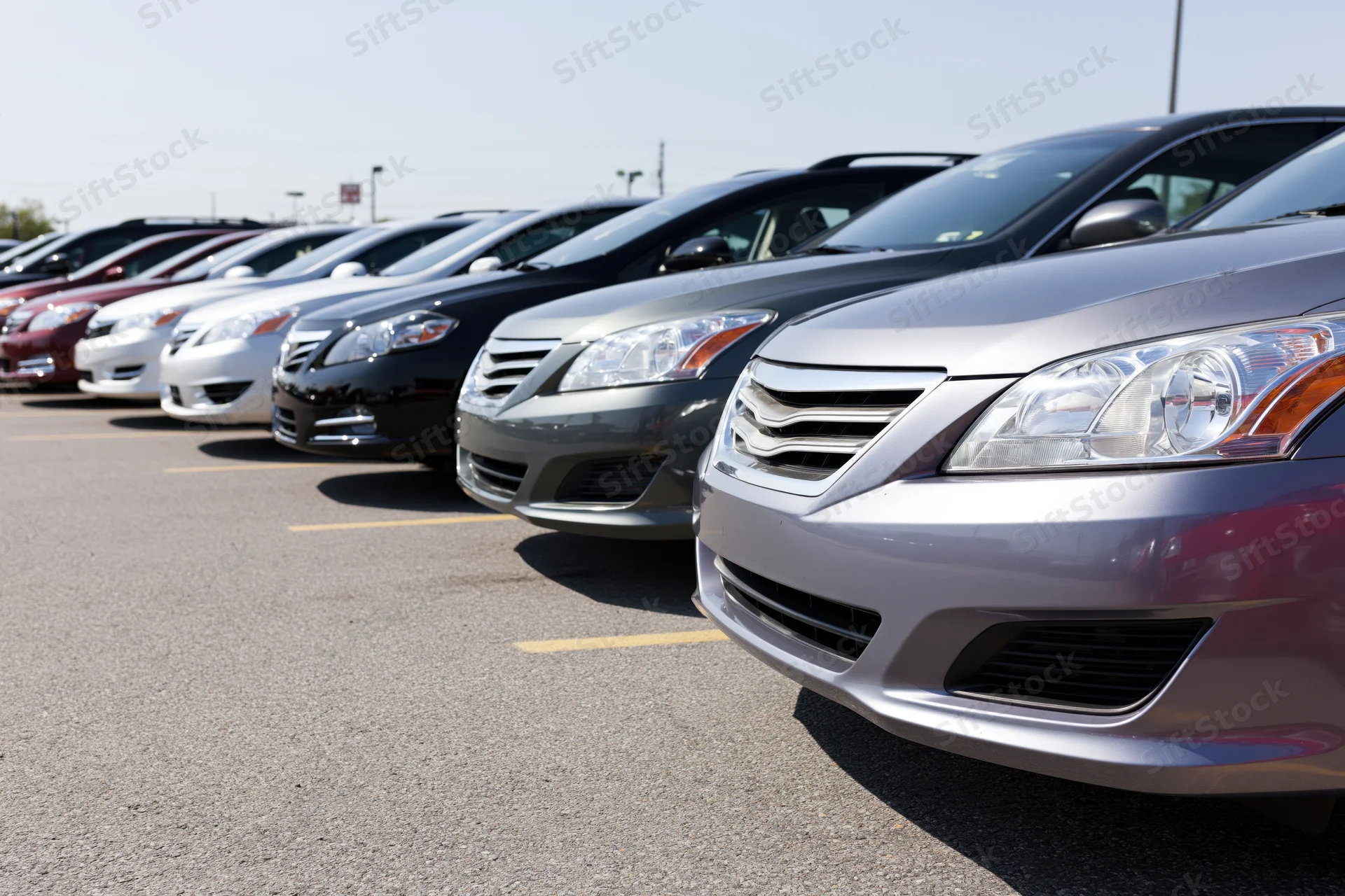 Row of sedans and hatchbacks parked diagonally in a dealership lot