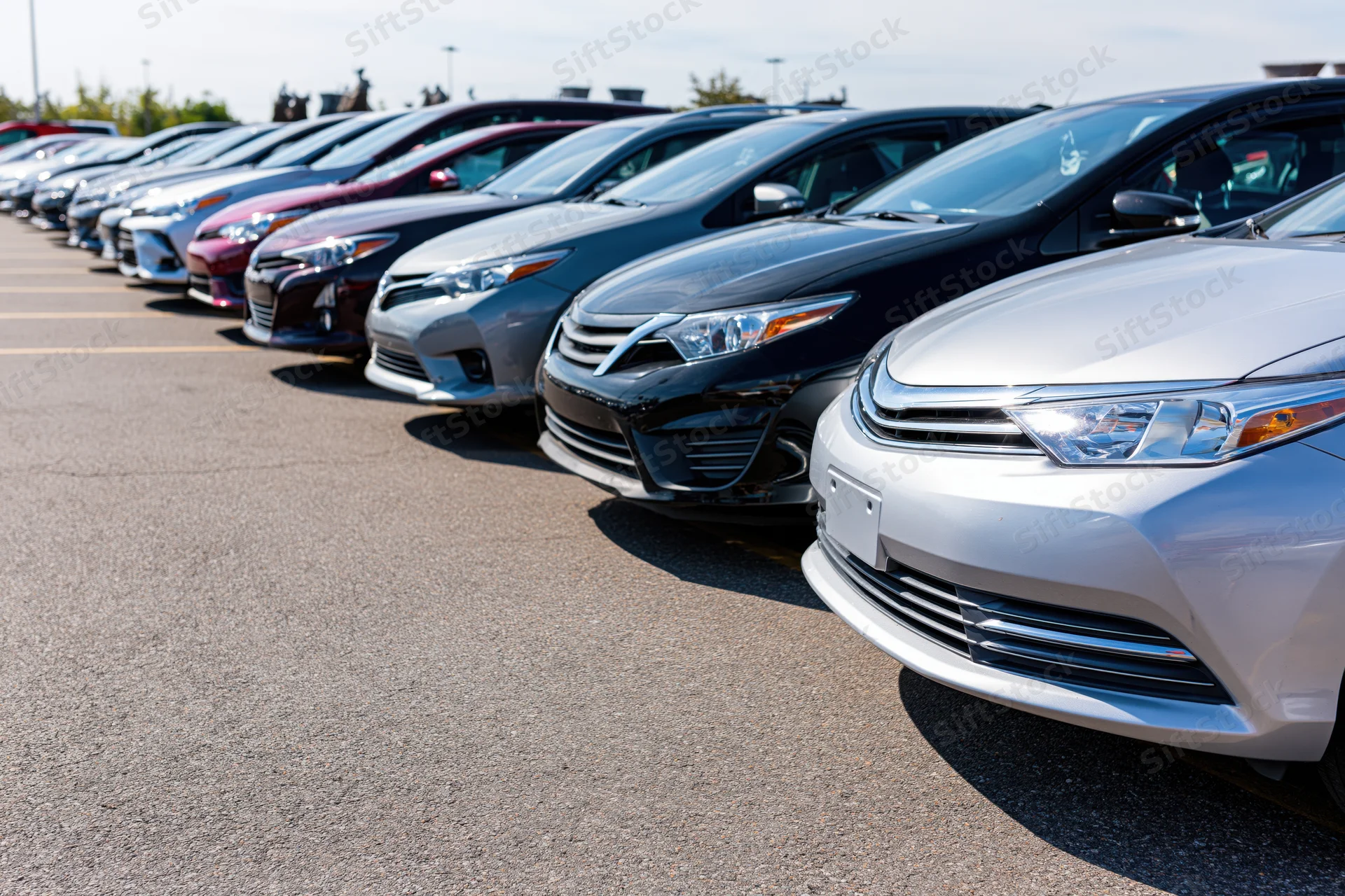 Row of sedans and hatchbacks parked diagonally in a dealership lot