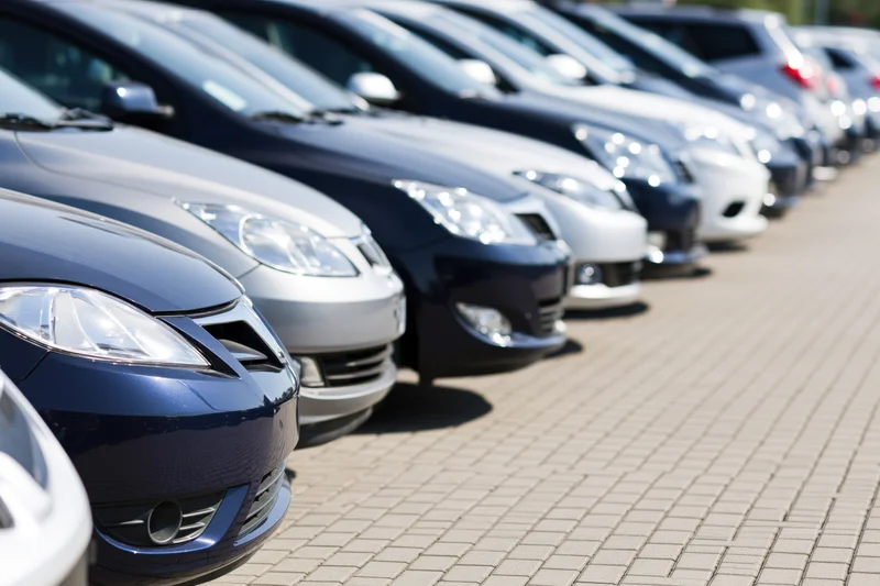 Row of sedans and hatchbacks parked diagonally on a brick pavement at a car dealership