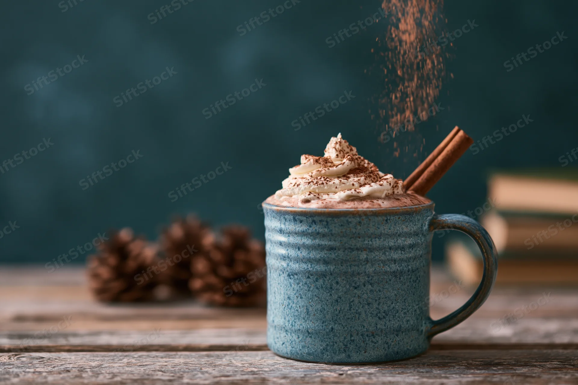 Blue ceramic mug filled with hot cocoa topped with whipped cream and cinnamon stick on wooden table