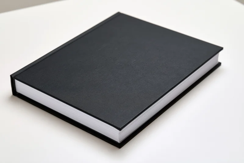 Black hardcover book with blank cover resting on white surface