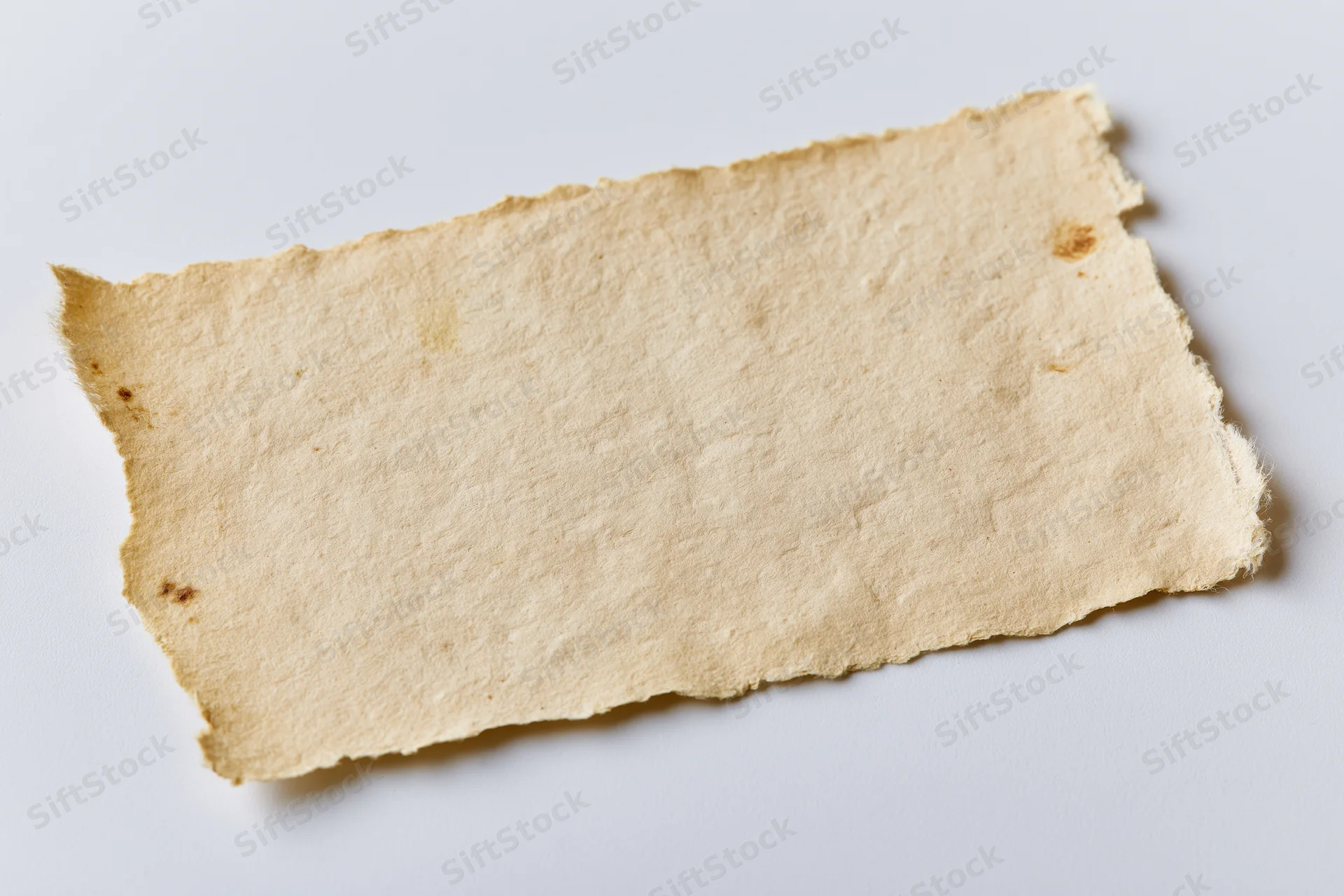 Torn aged paper fragment lying flat on white surface