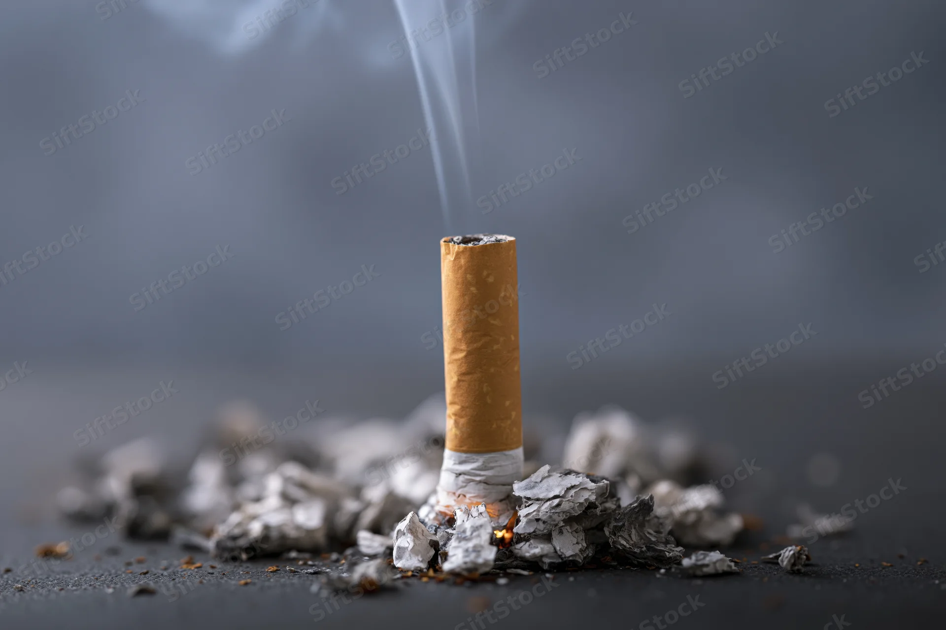 Cigarette butt smoldering upright in ash on dark surface