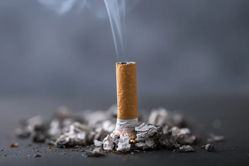 Cigarette butt smoldering upright in ash on dark surface