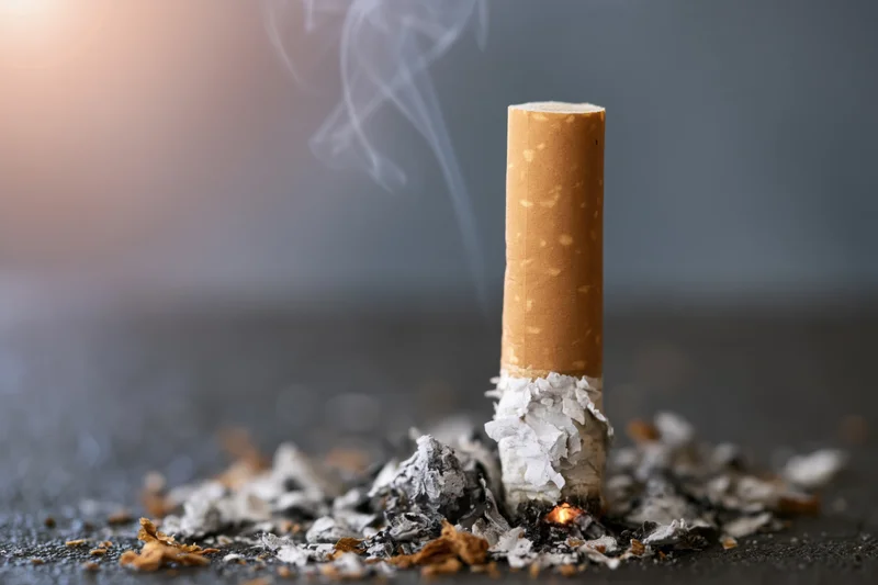 Cigarette butt with smoke rising from burning end on dark surface