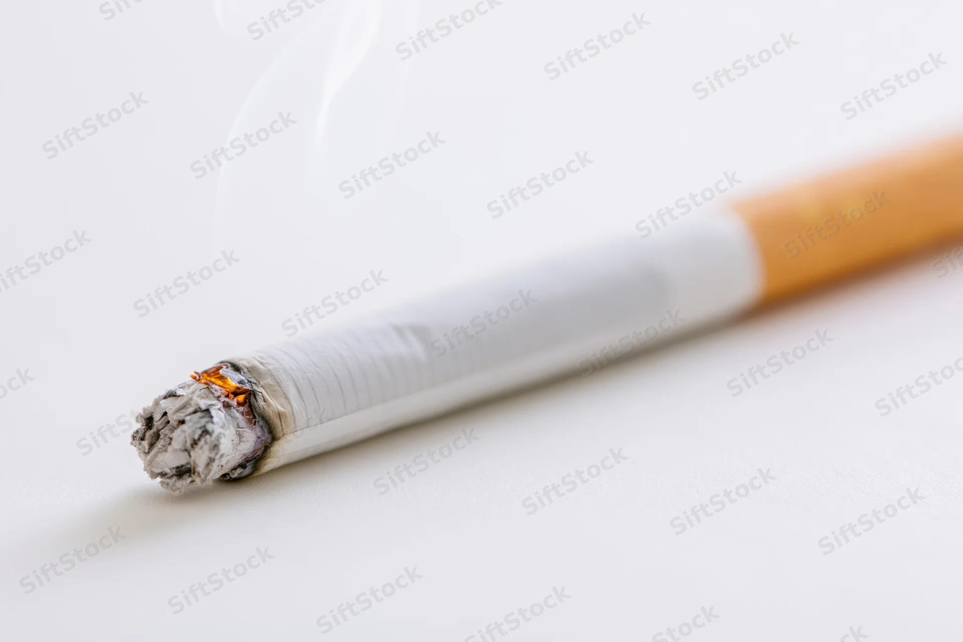 Lit cigarette burning with smoke rising on white surface
