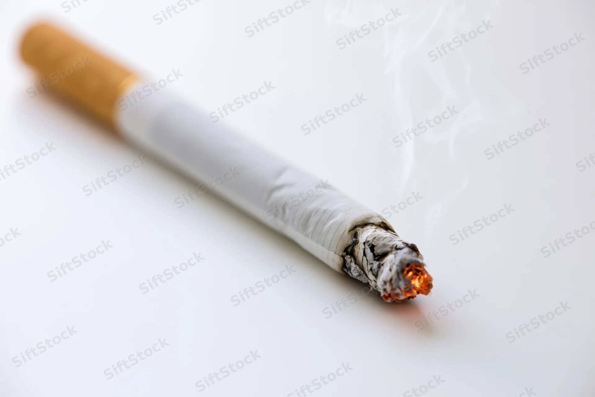 Lit cigarette burning with smoke rising on white background