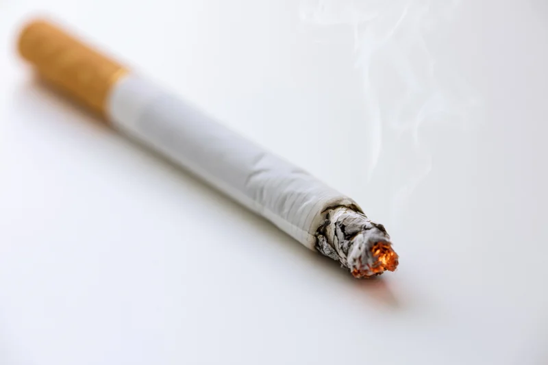 Single lit cigarette resting at a diagonal angle burning ember