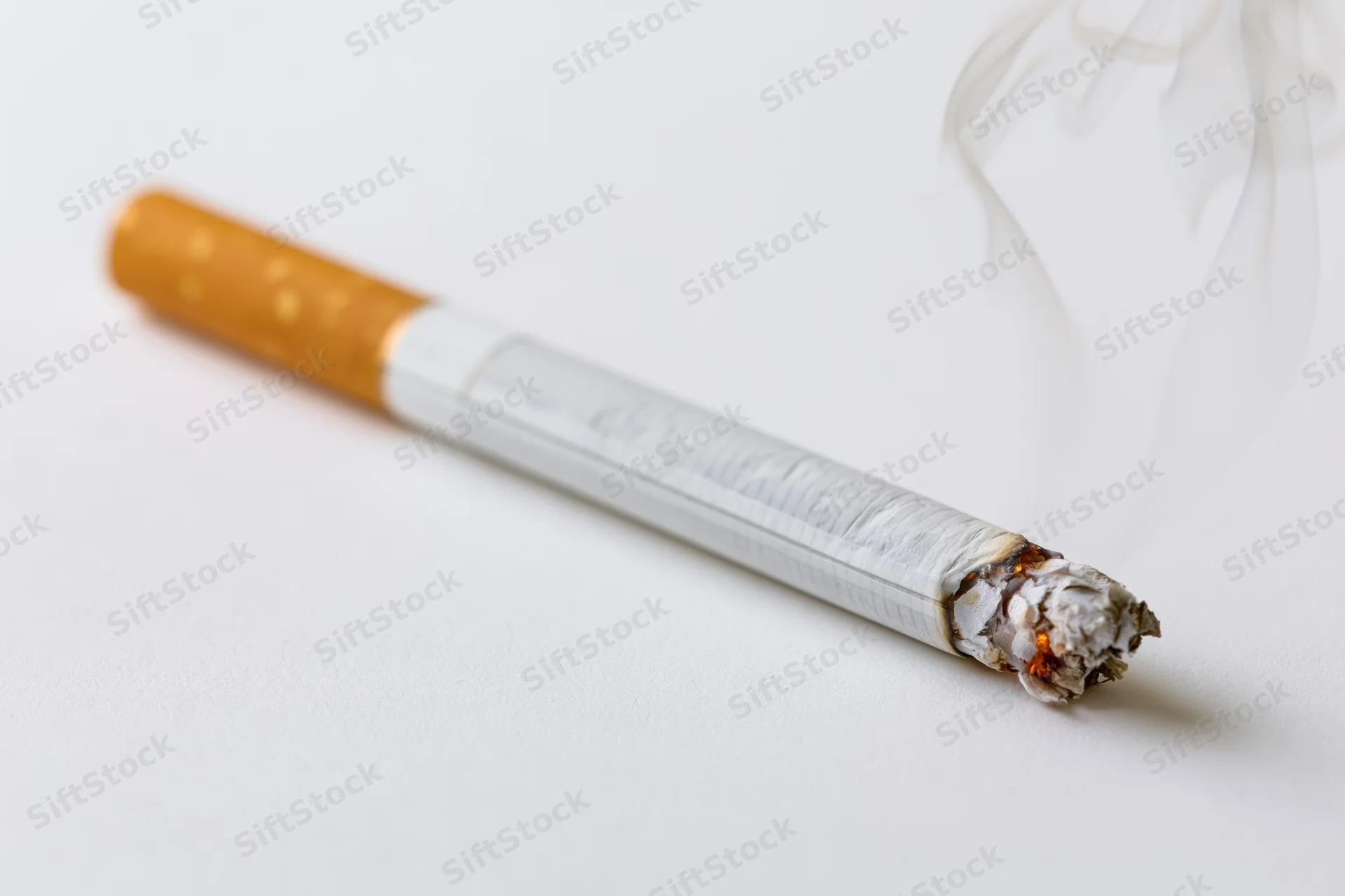 Lit cigarette burning with smoke and ash on white surface