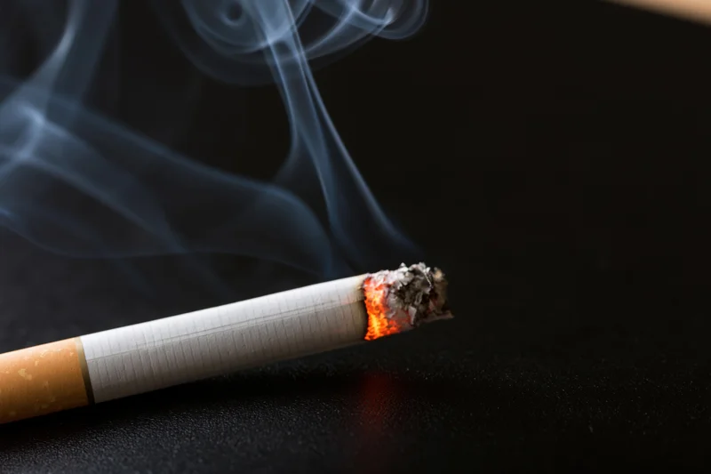 Lit cigarette burning with smoke rising on dark surface