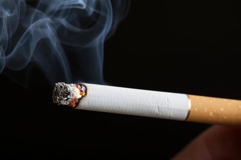 Lit cigarette with glowing ember and rising smoke held horizontally against black background