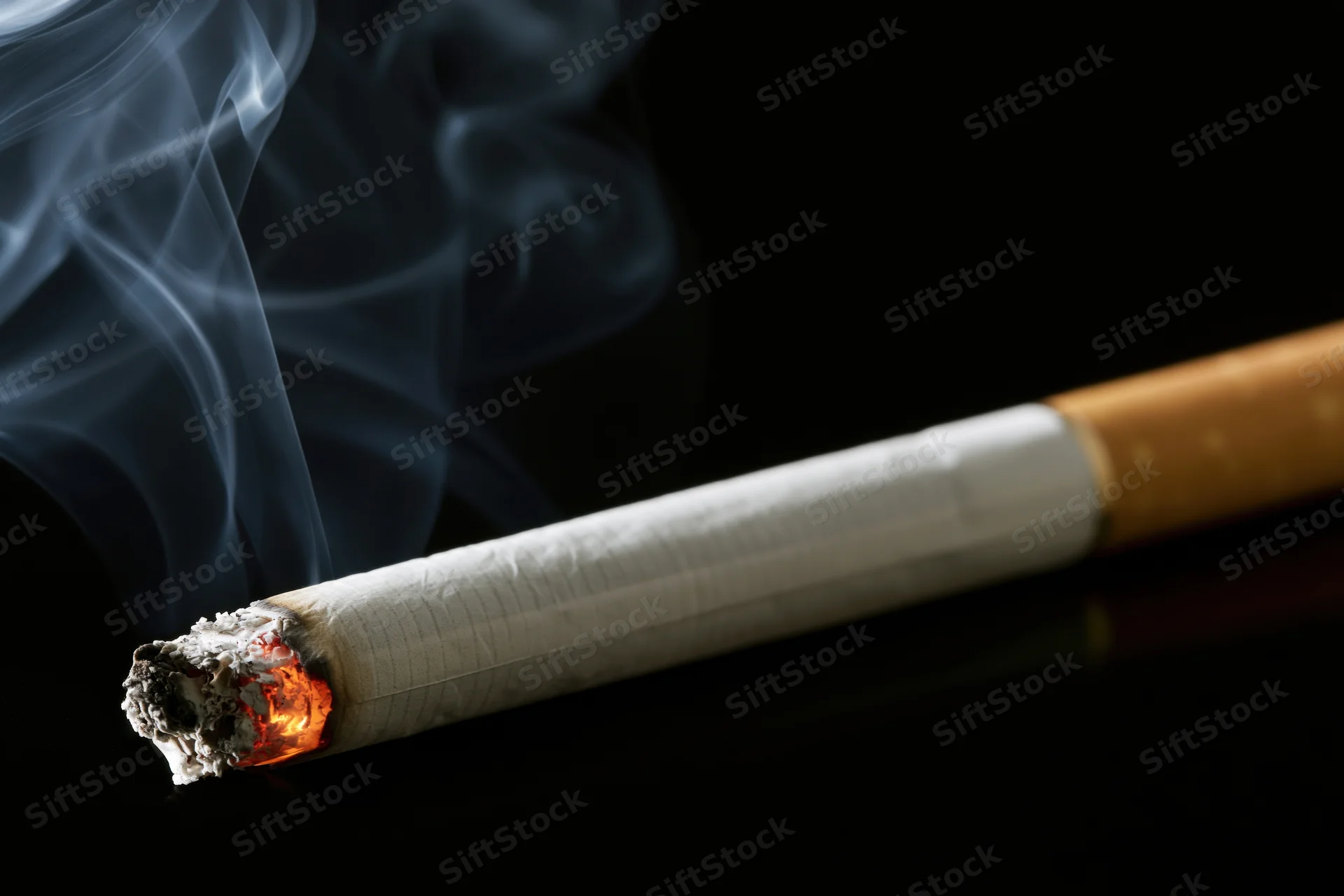 Lit cigarette with glowing ember and rising smoke on black surface